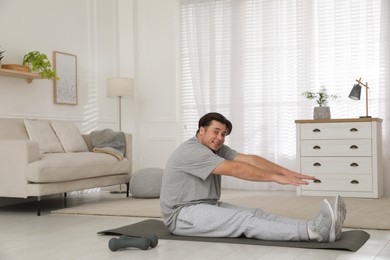 Overweight man stretching on mat at home, space for text