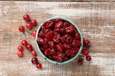 Photo of Tasty dried cranberries in bowl and fresh ones on rustic wooden table, top view