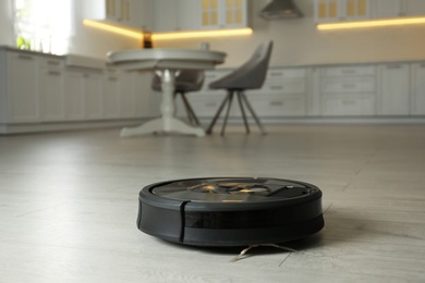 Modern robotic vacuum cleaner on floor in kitchen. Space for text