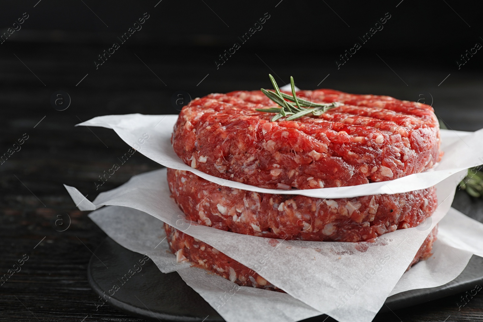 Photo of Raw meat cutlets for burger on black wooden table, closeup