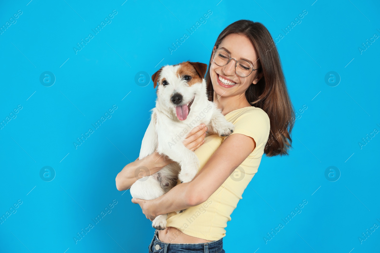 Photo of Young woman with her cute Jack Russell Terrier on light blue background. Lovely pet