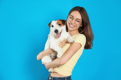 Photo of Young woman with her cute Jack Russell Terrier on light blue background. Lovely pet