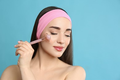 Photo of Woman using natural pink quartz face roller on light blue background