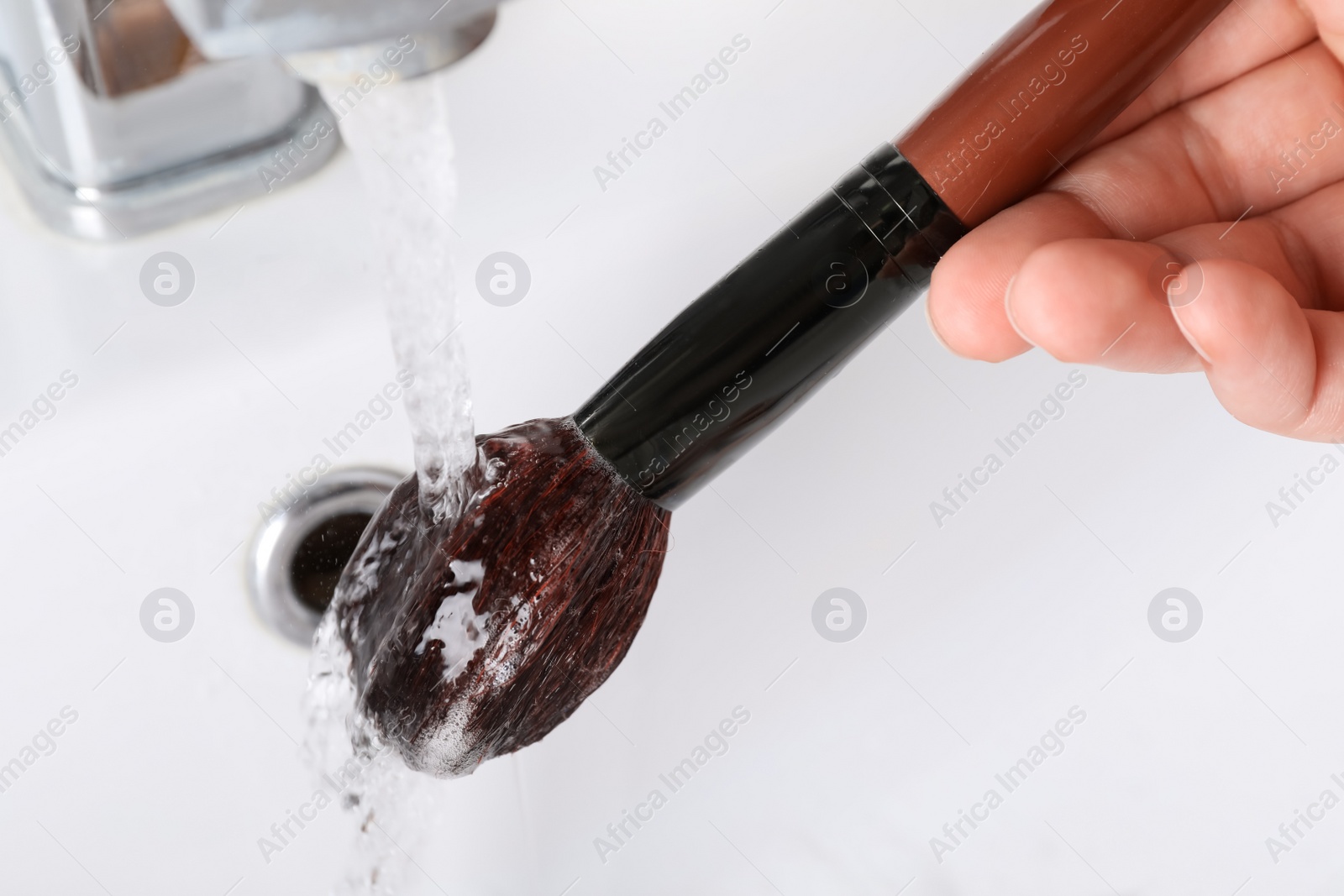 Photo of Woman washing makeup brush under stream of water in sink, closeup