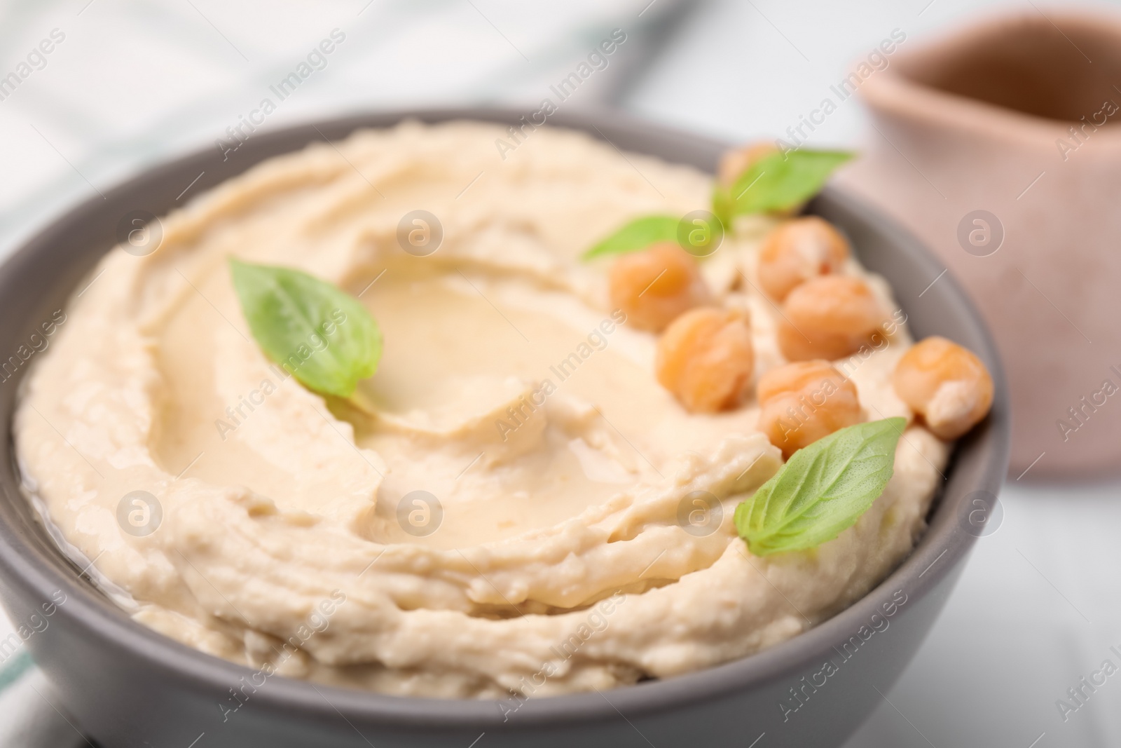 Photo of Delicious hummus with chickpeas served on white tiled table, closeup