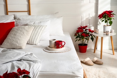 Photo of Poinsettias near bed in light cozy room. Christmas Interior design
