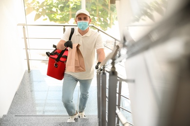 Photo of Courier in protective mask and gloves with order indoors. Restaurant delivery service during coronavirus quarantine