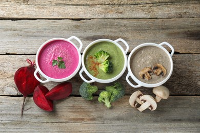 Photo of Different tasty cream soups in bowls and ingredients on old wooden table, flat lay