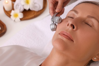 Photo of Woman receiving facial massage with metal roller in beauty salon, closeup