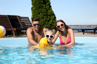 Photo of Happy family with inflatable ring in outdoor swimming pool on sunny summer day