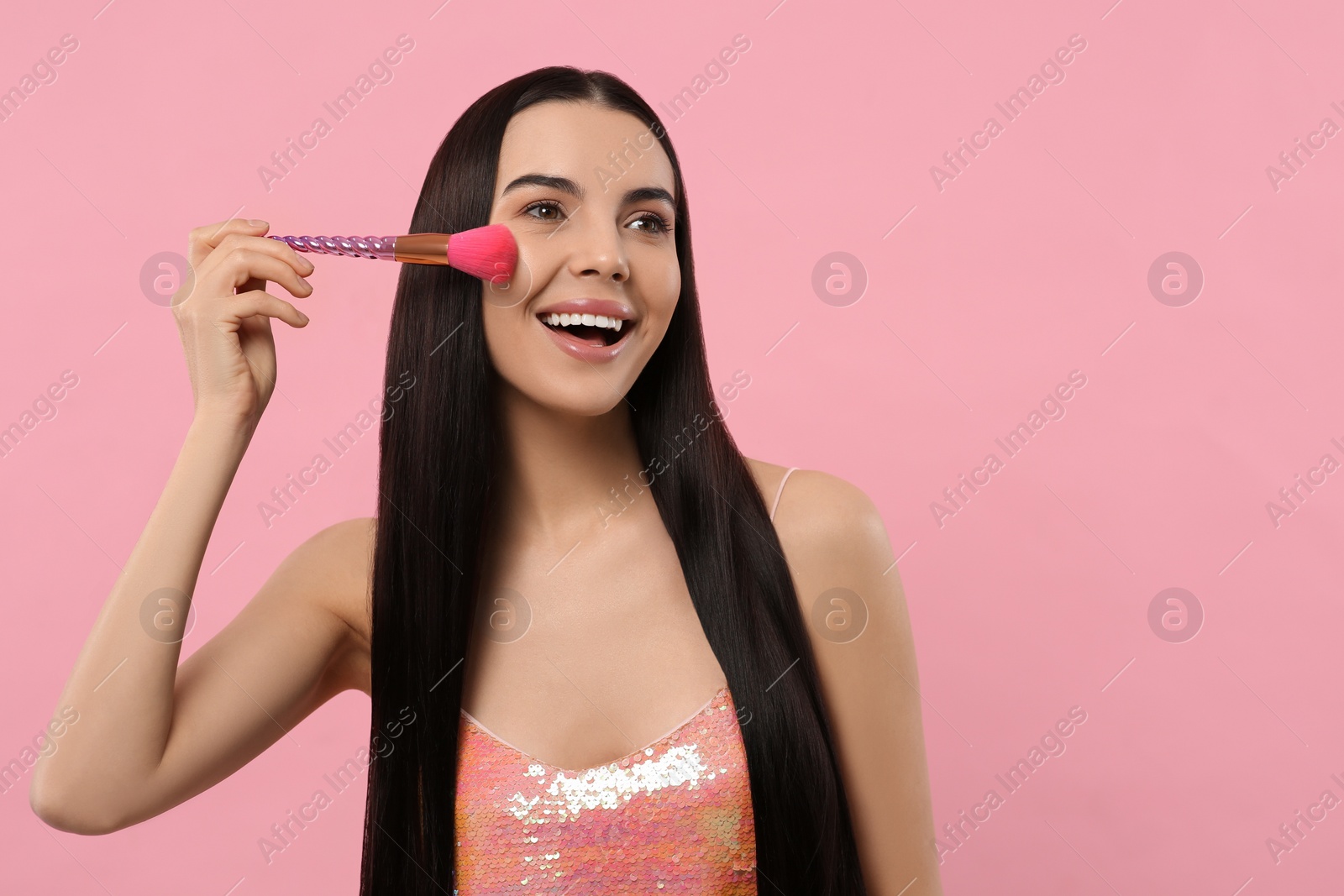 Photo of Beautiful woman applying makeup with brush on pink background, space for text