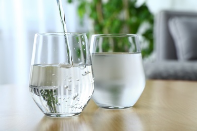 Photo of Pouring water into glass on wooden table. Refreshing drink