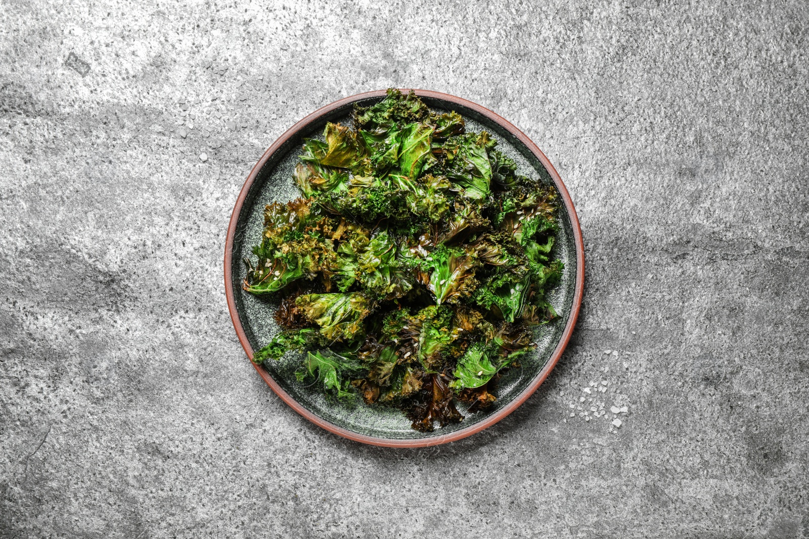 Photo of Tasty baked kale chips on grey table, top view