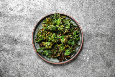 Photo of Tasty baked kale chips on grey table, top view