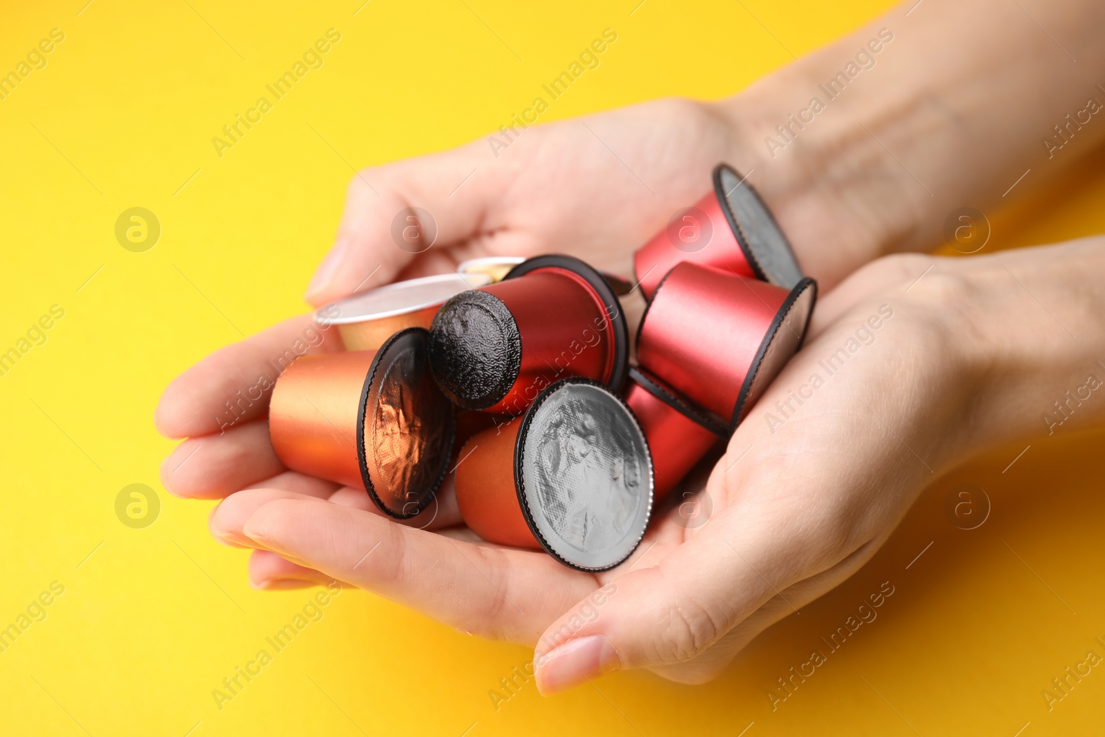 Photo of Woman holding heap of coffee capsules on yellow background, closeup