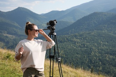 Photo of Professional photographer with modern camera on tripod in mountains. Space for text