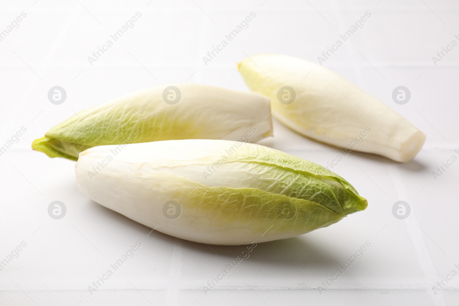 Photo of Fresh raw Belgian endives (chicory) on white tiled table