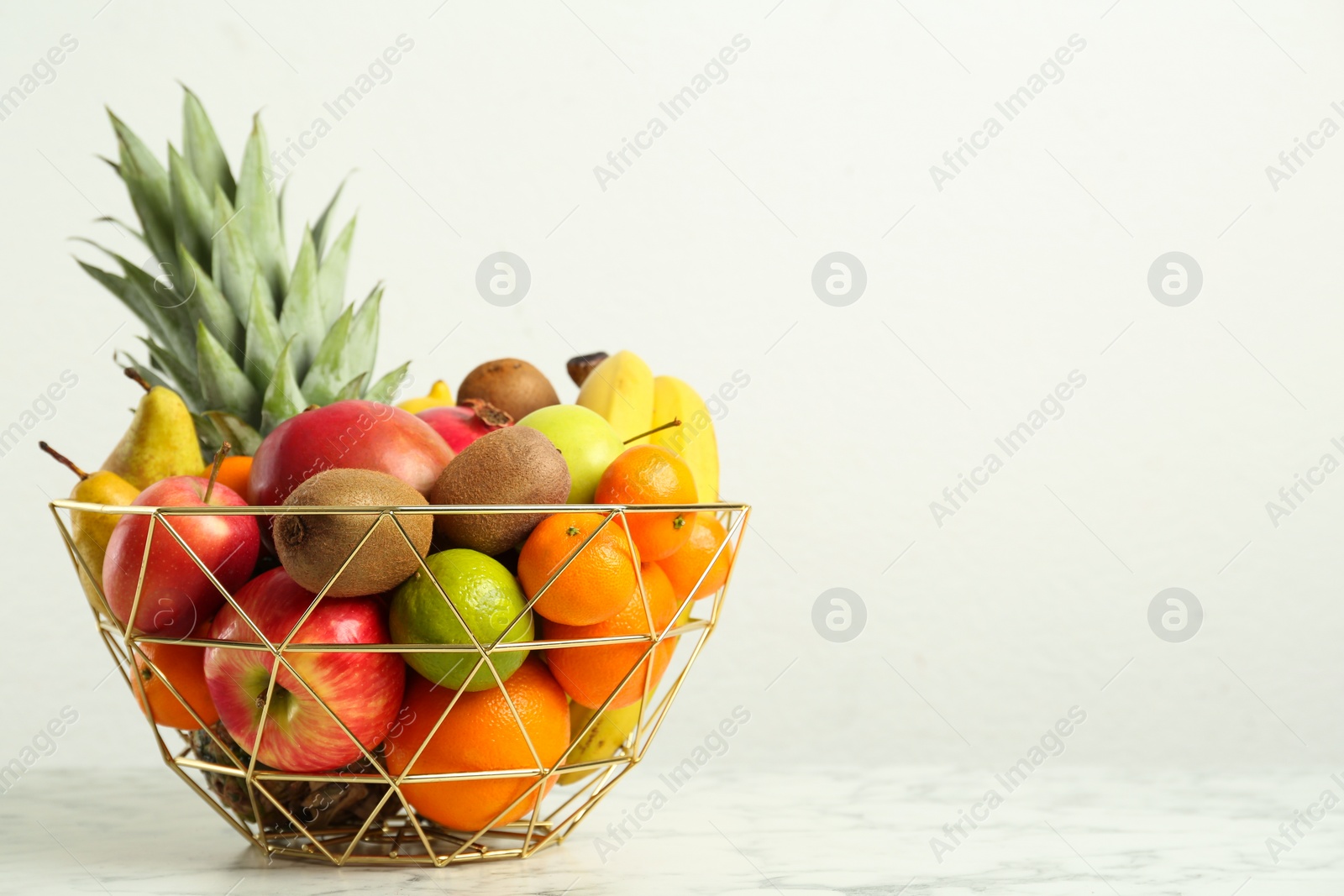 Photo of Metal bowl with different fresh fruits on white marble table. Space for text