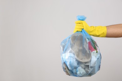 Man holding full garbage bag on light background, closeup. Space for text