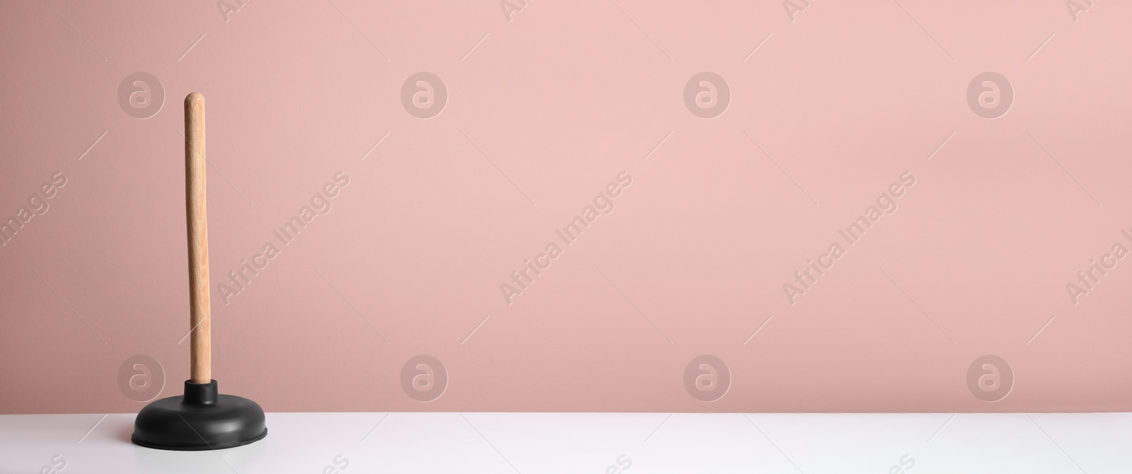 Photo of Plunger on white table against pink background. Space for text