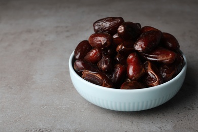 Photo of Bowl with sweet dates on grey background, space for text. Dried fruit as healthy snack
