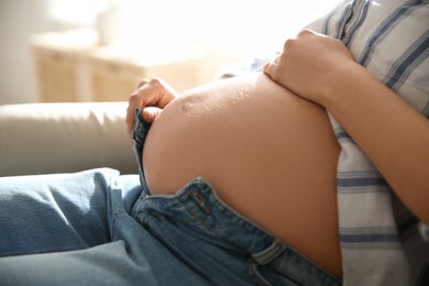 Photo of Pregnant woman touching her belly indoors, closeup