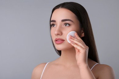 Photo of Beautiful woman removing makeup with cotton pad on gray background, space for text