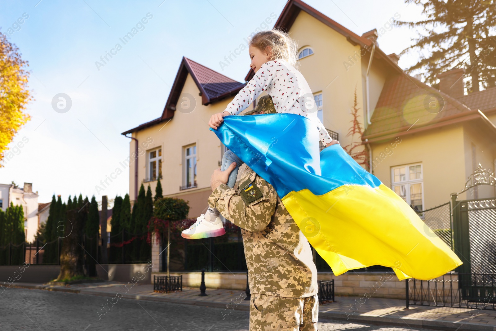 Photo of Soldier in military uniform carrying his daughter on shoulders and Ukrainian flag on city street, space for text. Family reunion