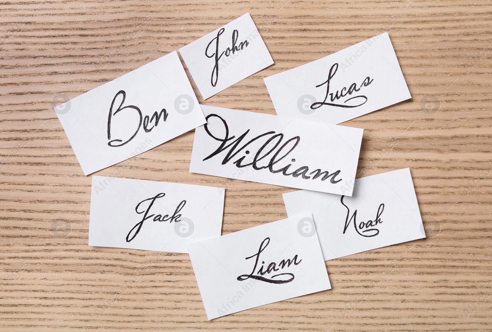 Photo of Paper sheets with written baby names on wooden table, flat lay