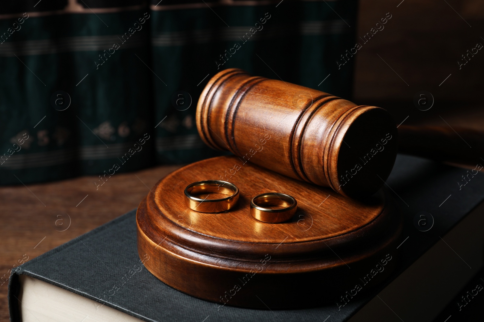 Photo of Divorce concept. Gavel, wedding rings and book on wooden table, closeup