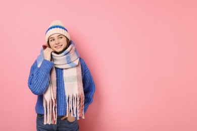 Beautiful woman in warm scarf and hat on pink background, space for text