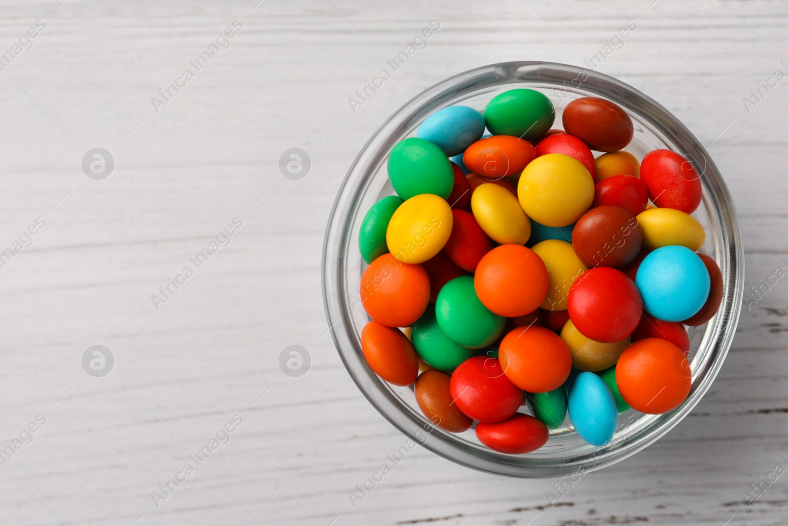 Photo of Bowl with tasty colorful candies on white wooden table, top view. Space for text