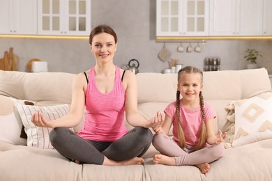 Photo of Happy mother with daughter meditating on sofa at home. Harmony and zen