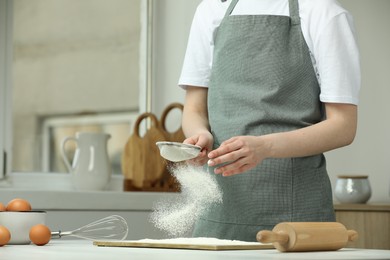 Photo of Woman sieving flour at table in kitchen, closeup. Space for text