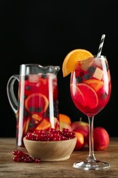 Photo of Glass and jug of Red Sangria with fruits on wooden table against black background
