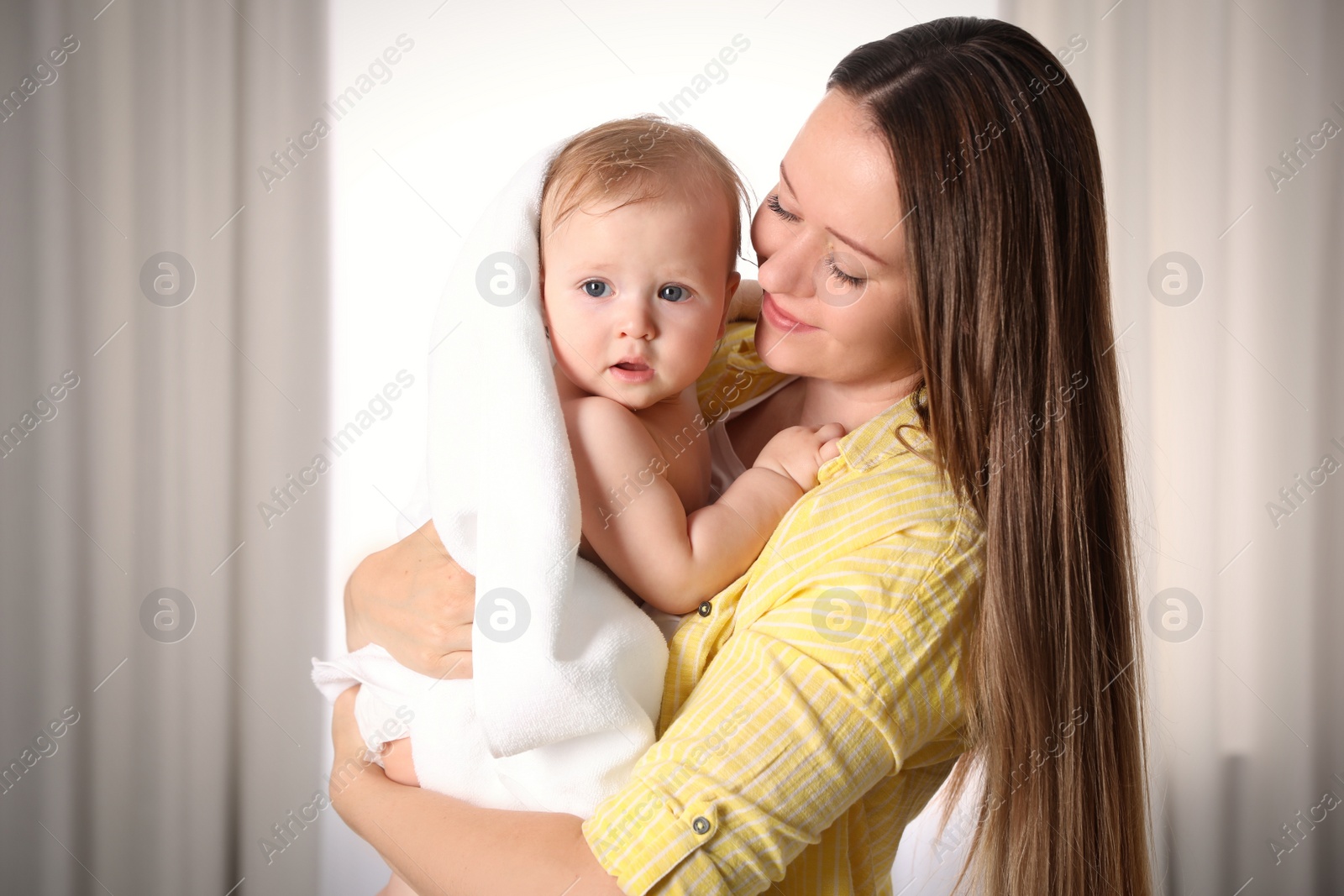 Photo of Mother holding cute little baby wrapped with towel indoors after bath