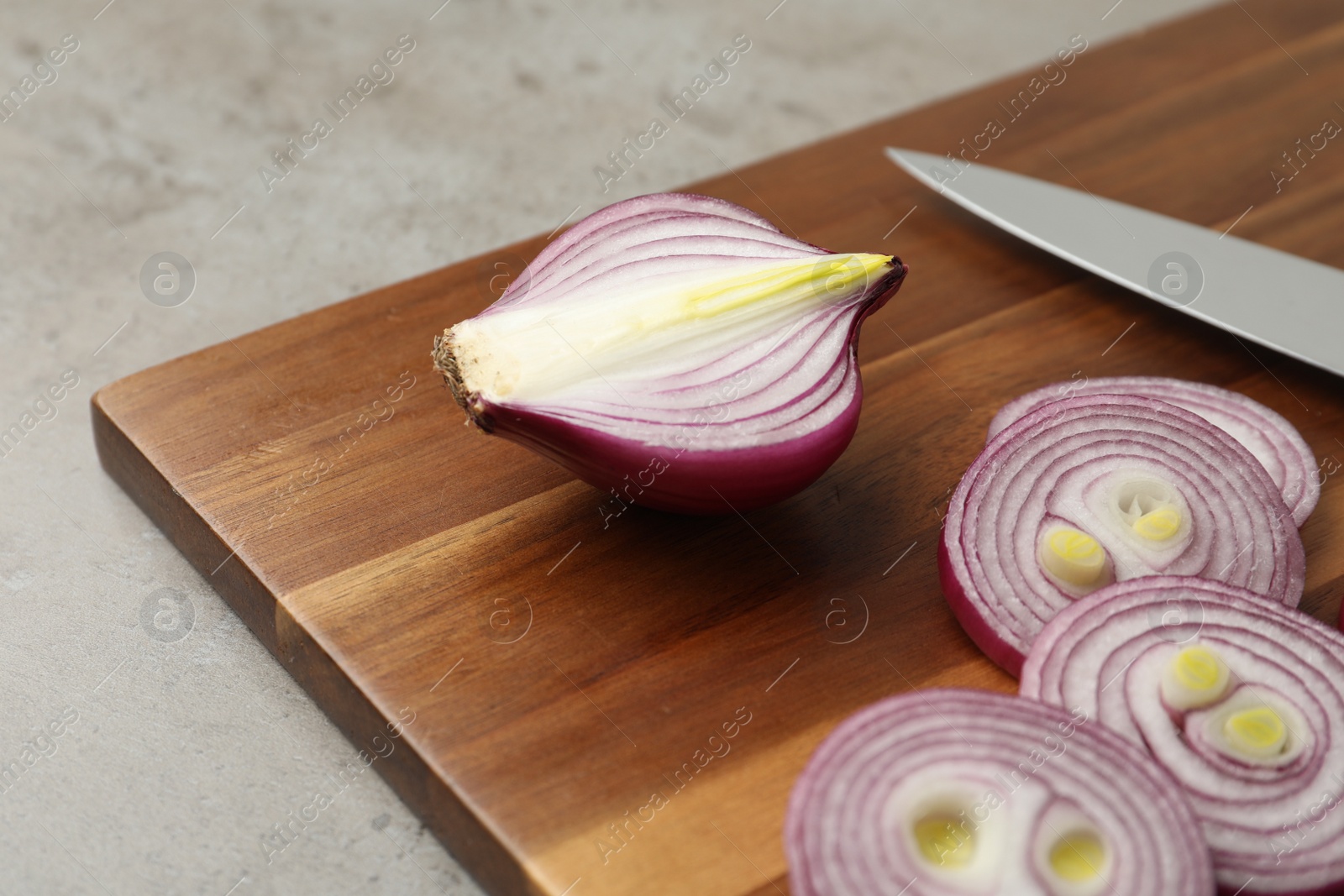 Photo of Cut red onion and wooden board on light grey table, closeup