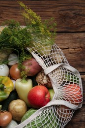 Photo of Different fresh vegetables in net bag on wooden table, top view. Farmer harvesting