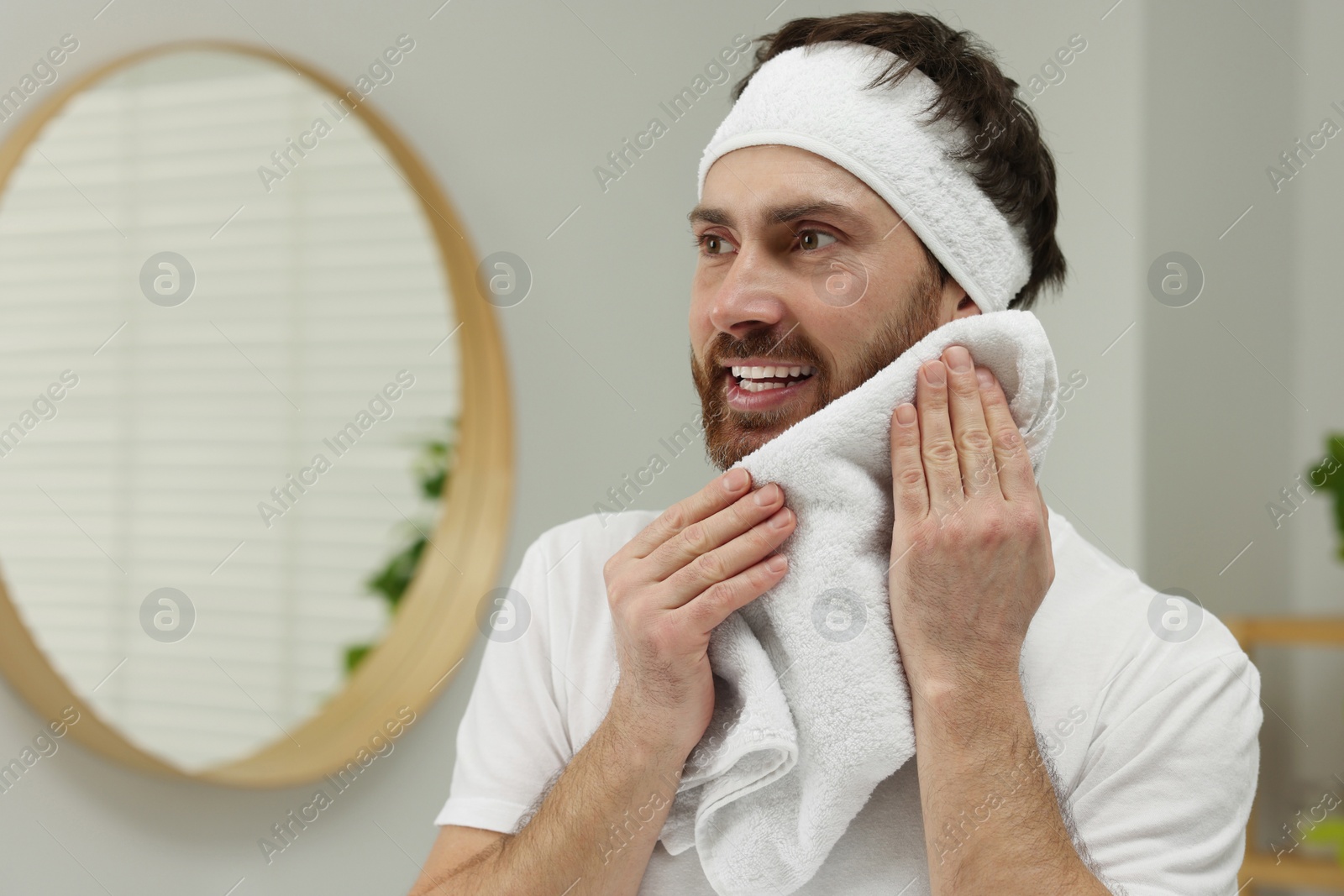 Photo of Washing face. Man with headband and towel in bathroom