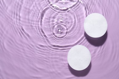Photo of Cotton pads in micellar water on violet background, top view. Space for text