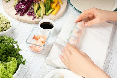 Photo of Woman making rice paper roll at white wooden table, closeup