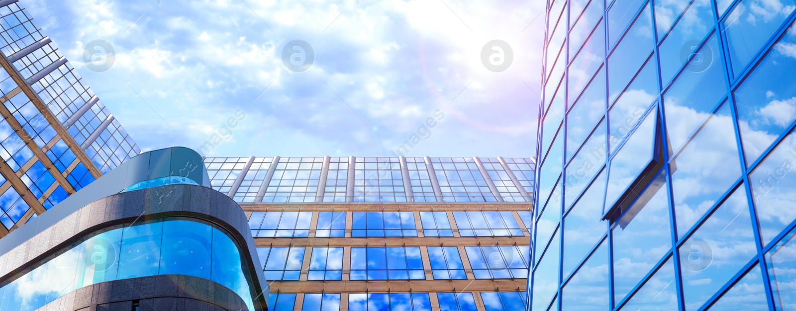 Image of Beautiful blue sky with clouds reflecting in windows of modern buildings, low angle view. Banner design