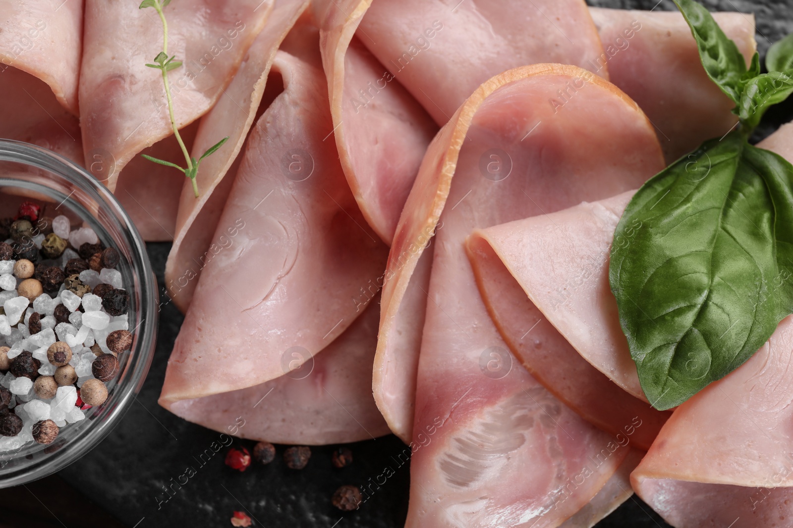 Photo of Tasty ham with basil, peppercorns and sea salt on black board, closeup