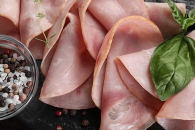 Photo of Tasty ham with basil, peppercorns and sea salt on black board, closeup