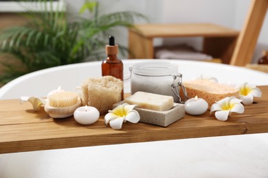 Photo of Composition with different spa products and beautiful flowers on tub tray in bathroom