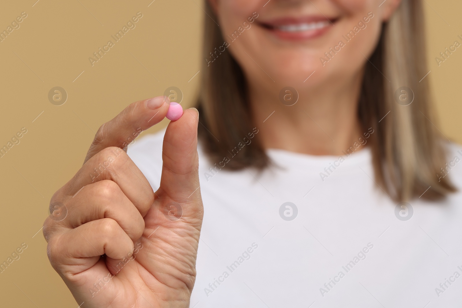 Photo of Senior woman with pill on beige background, closeup