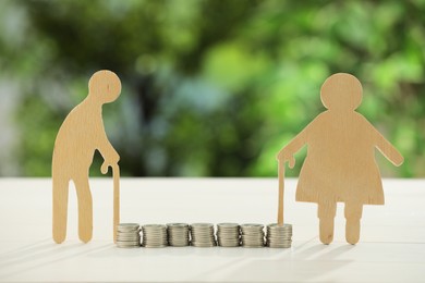 Pension savings. Figures of senior couple and coins on white table against blurred green background