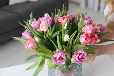 Photo of Woman putting bouquet of beautiful tulips in vase indoors, closeup