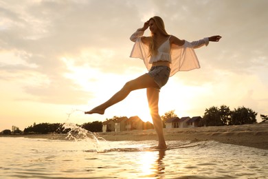 Beautiful young woman playing with water on sea beach