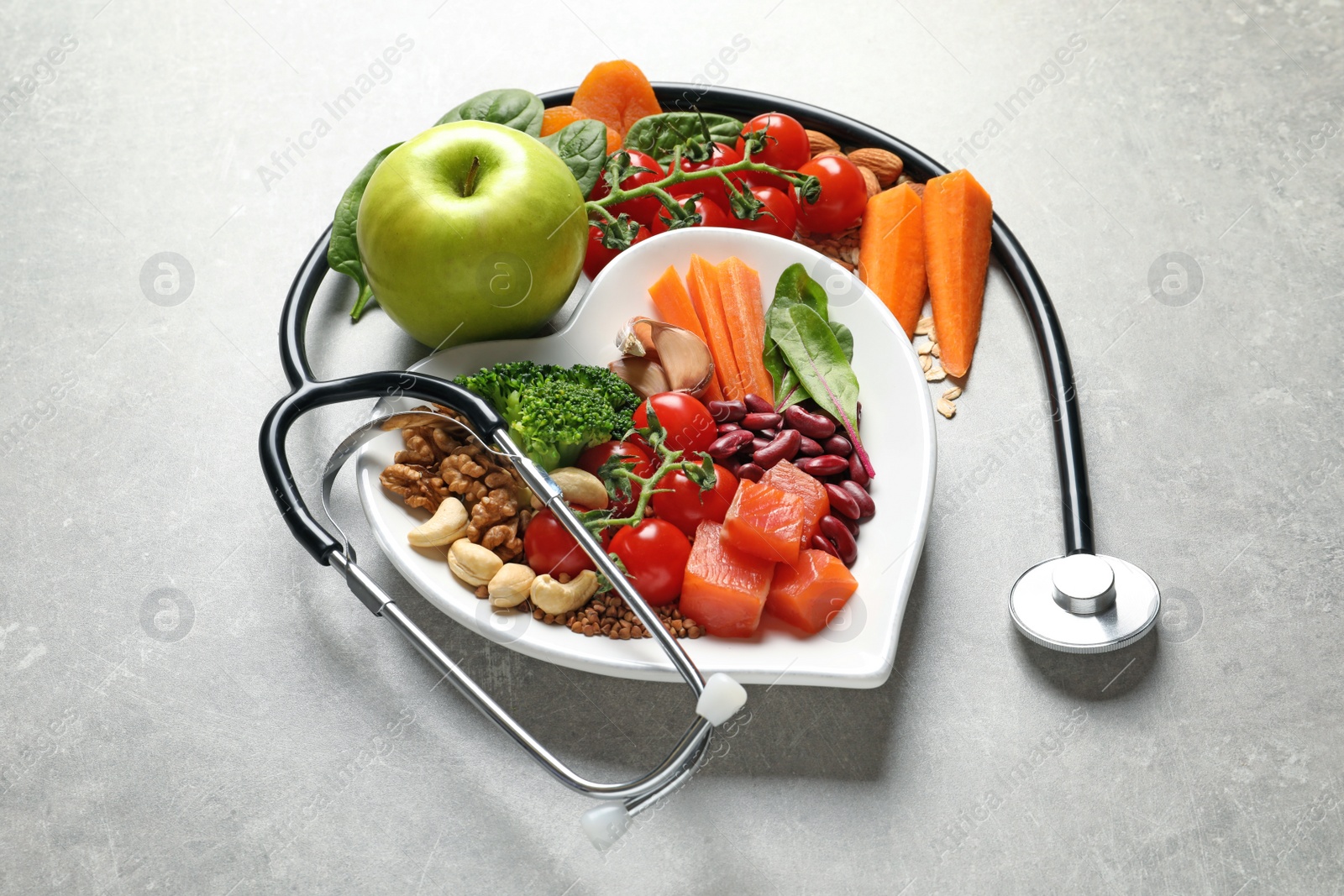 Photo of Plate of products for heart-healthy diet and stethoscope on grey table